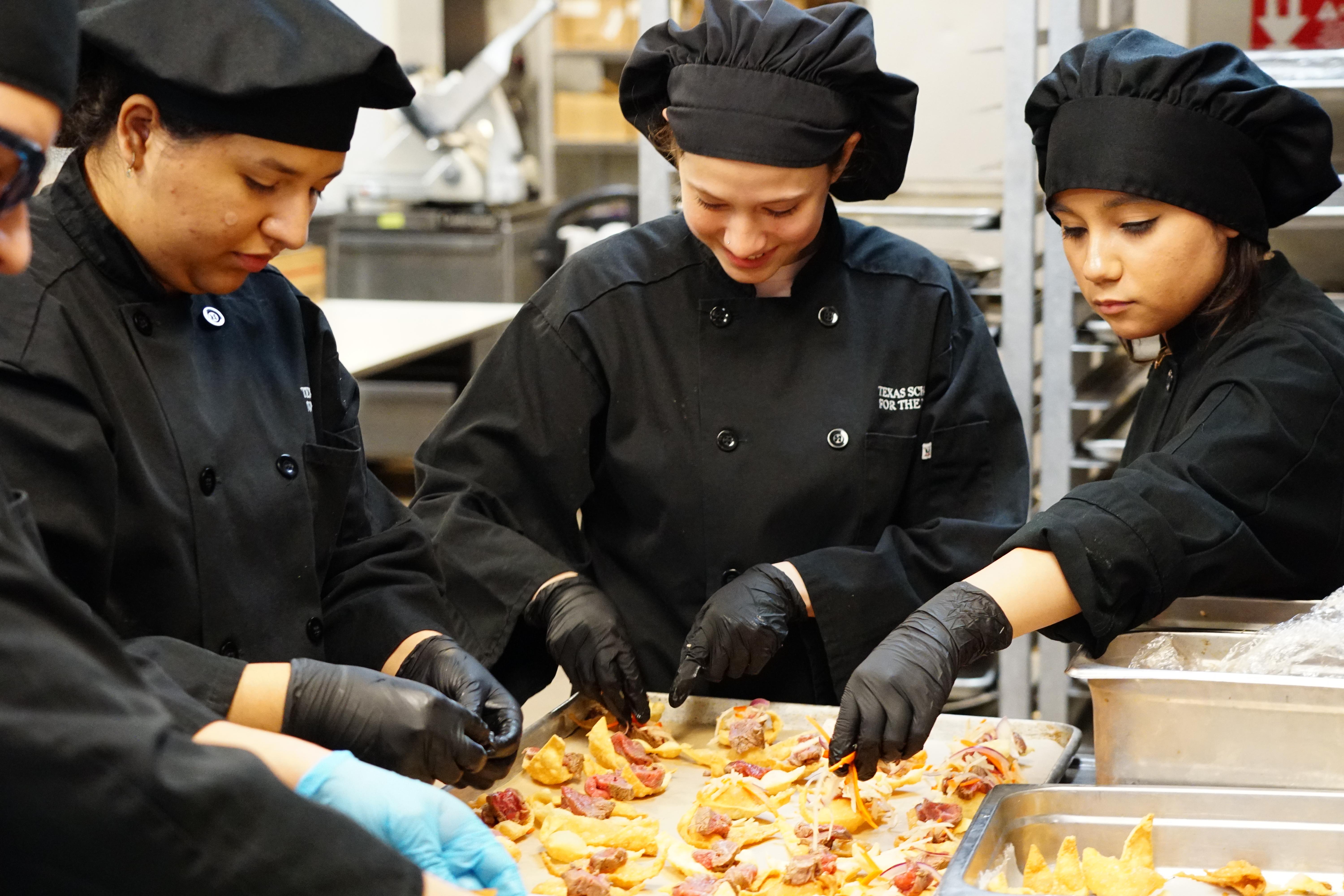 three culinary students with black chef hats and uniforms incorporating the appetizer meal for the Gala.