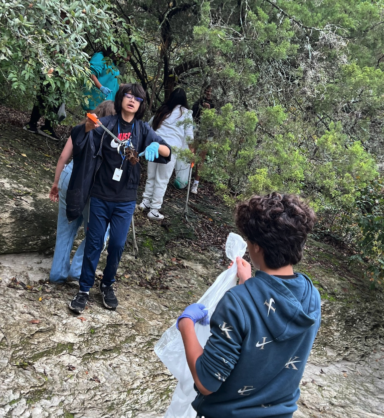 One middle schooler picked up the trash with the trash grabber. Another middle schooler held the trash bag at the creek.