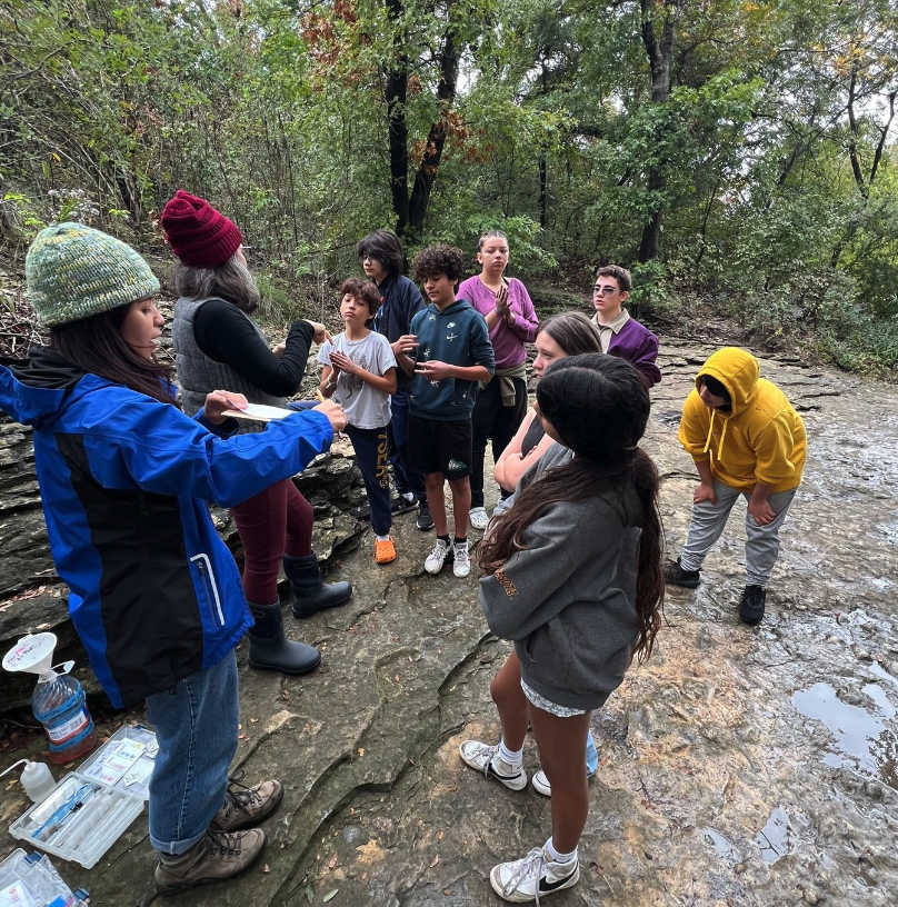 A staff from Keep Austin Beautiful explains about the watersheds to middle school students at a creek.