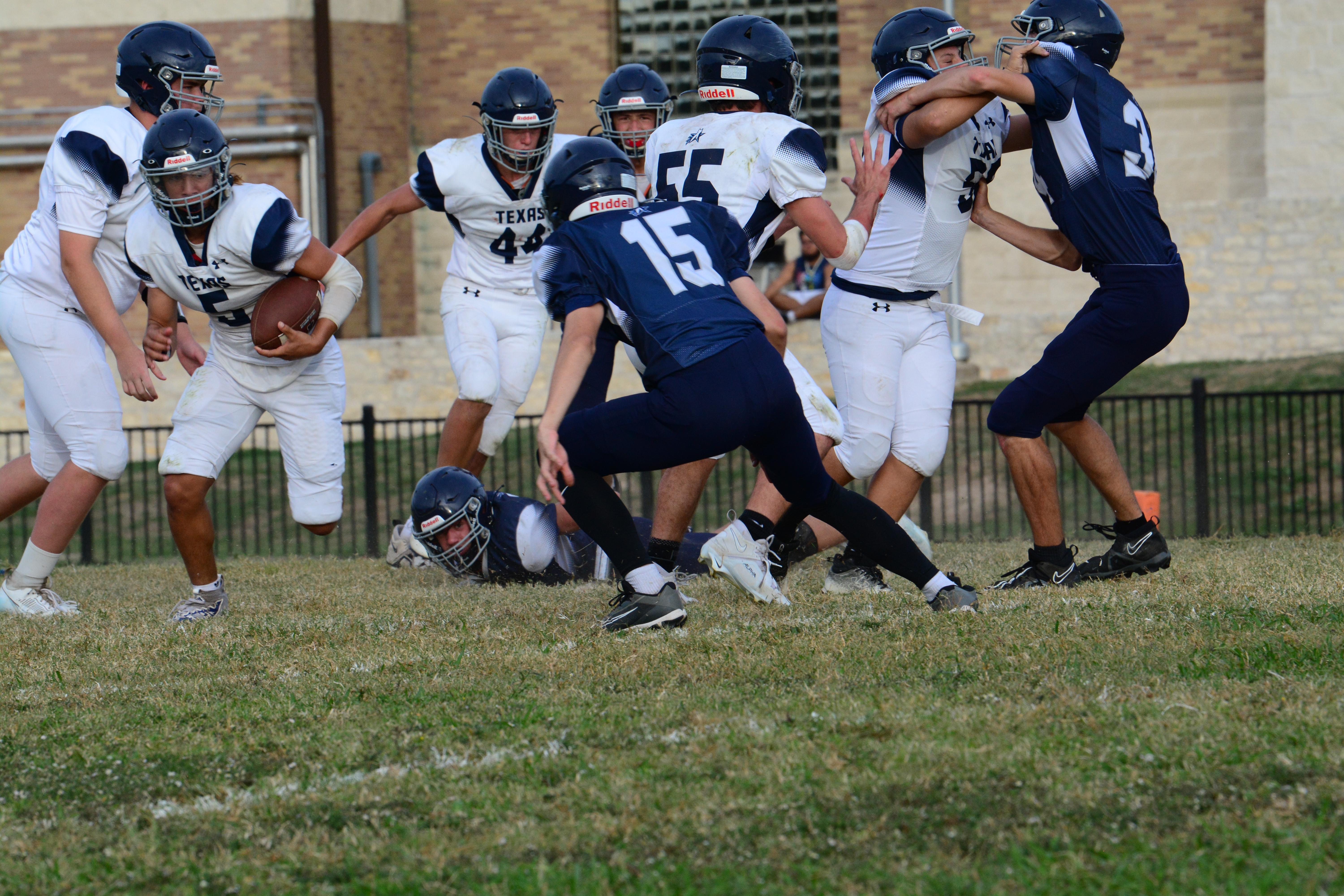  6 white uniforms football athletes on the field, three blue uniforms played defense, and the number 5 is holding the ball. On the far right, blue and white uniforms tackled each other.