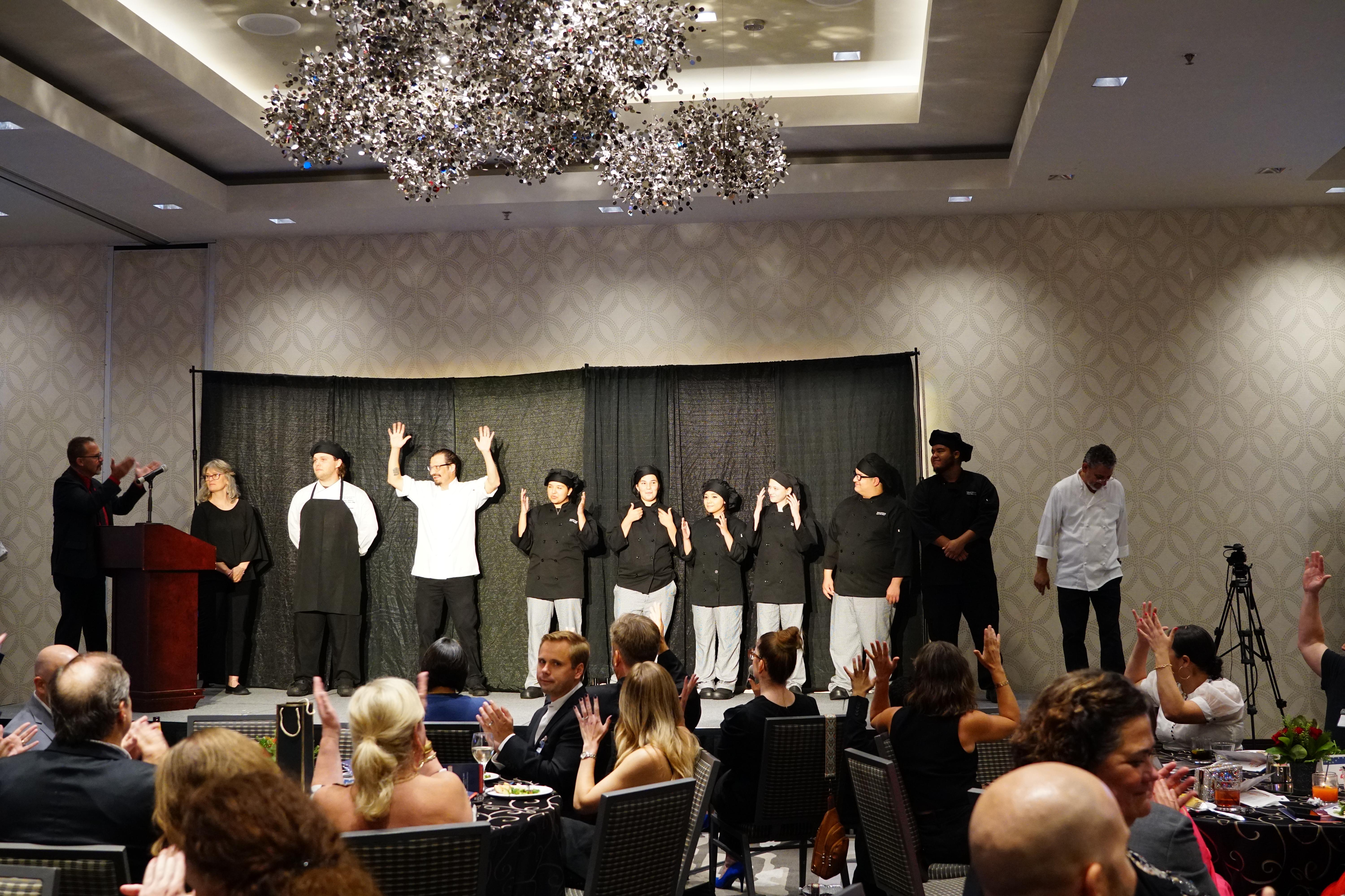  Peter Bailey introduces the culinary students to the Diamond Gala. Far left: Peter Bailey, an interpreter, chef from Sonstra, culinary teacher, six culinary students, culinary teacher assistant on the stage. 